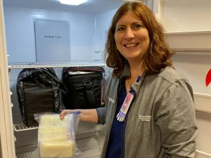 Nurse holding ziploc bag of donated milk in milk storage bags in front of freezer.
