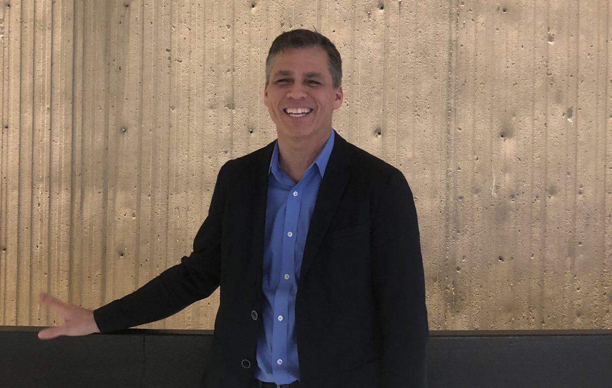 Jeffrey Taylow standing in black blazer with blue button up shirt on a wood background